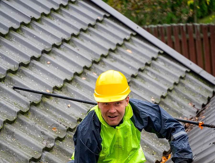 Worker in hi-vis clearing a roof gutter
